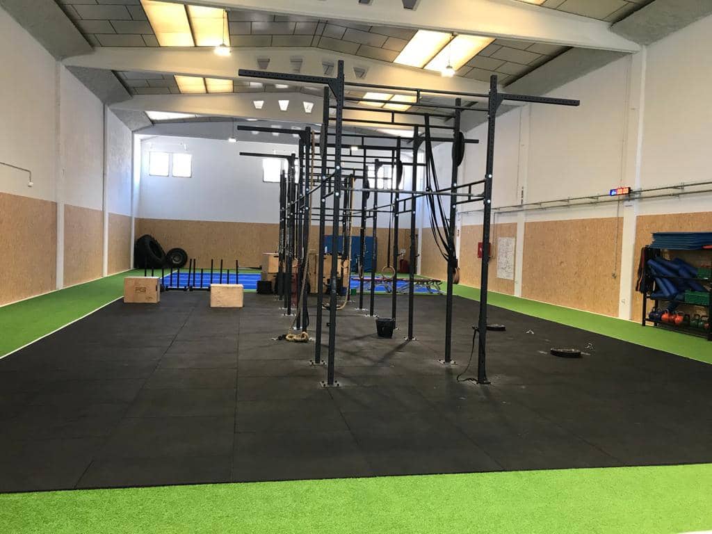 Pavimento deportivo completo con losetas de caucho de alta densidad y pista de césped artificial en nave industrial.